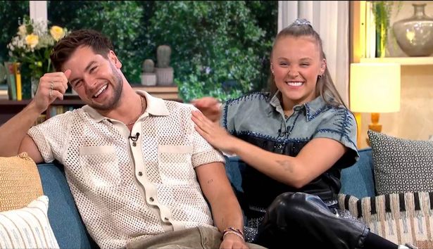Chris Hughes, em uma calça bege e marrom, sentou -se ao lado de JoJo Siwa, em uma blusa azul e preta, e calças pretas, no sofá nesta manhã.