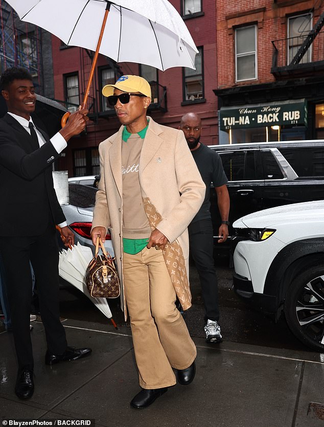 Pharrell Williams usava um sobretudo de caxemira bronzeado de comprimento médio que deixou desabotoado e se abriu apenas o suficiente para revelar que o padrão clássico da Louis Vuitton decorando o forro