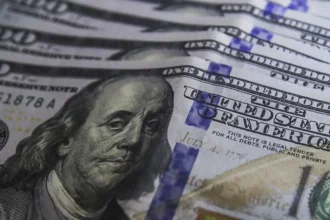 Cédulas de dólar e moedas de real, símbolo da variação cambial