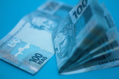 Pilha de cédulas de 100 reais sobre superfície azul, ilustrando a inflação medida pelo IPCA-15